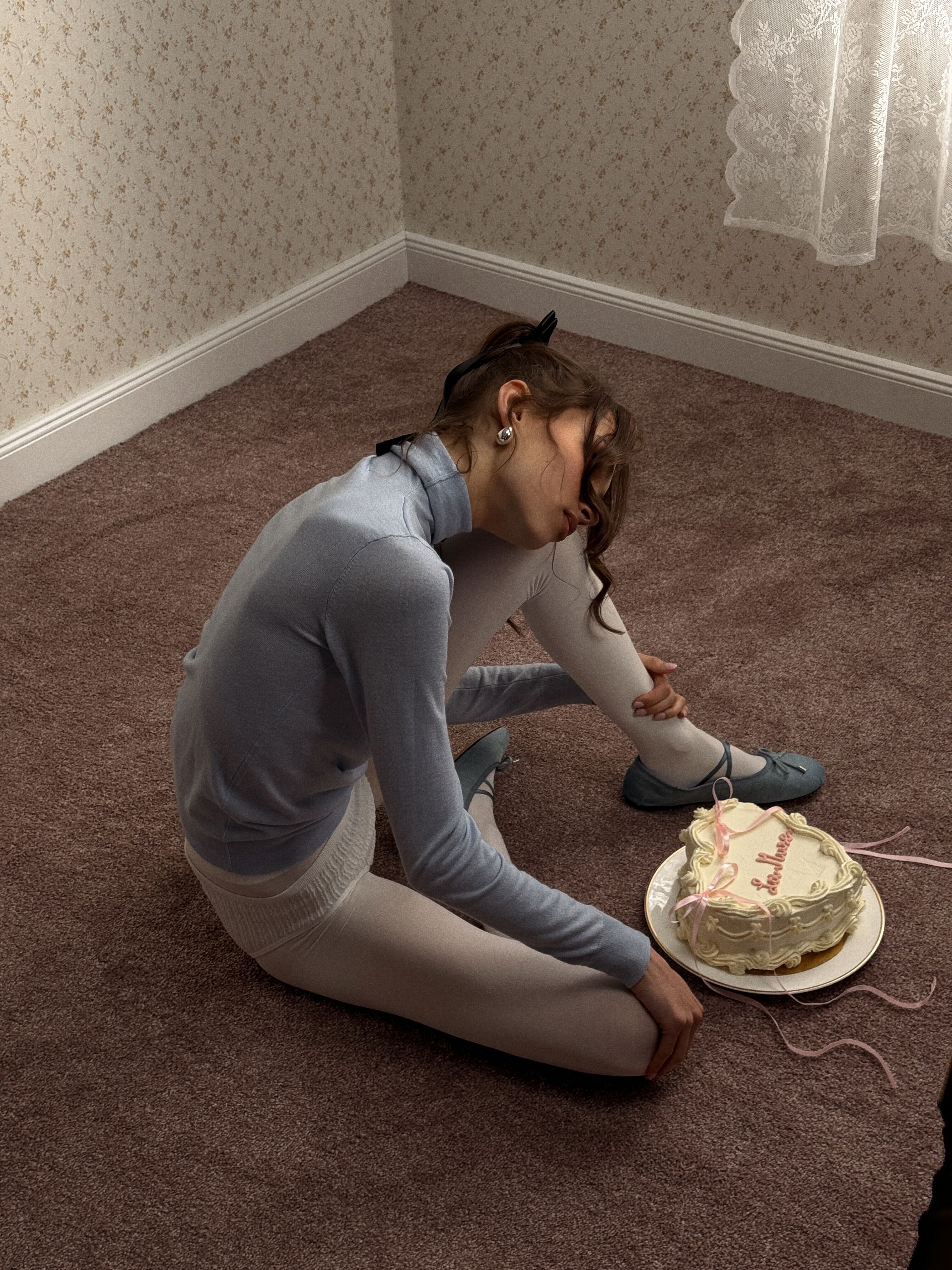 Dreamy woman sitting on floor next to a delicious cake