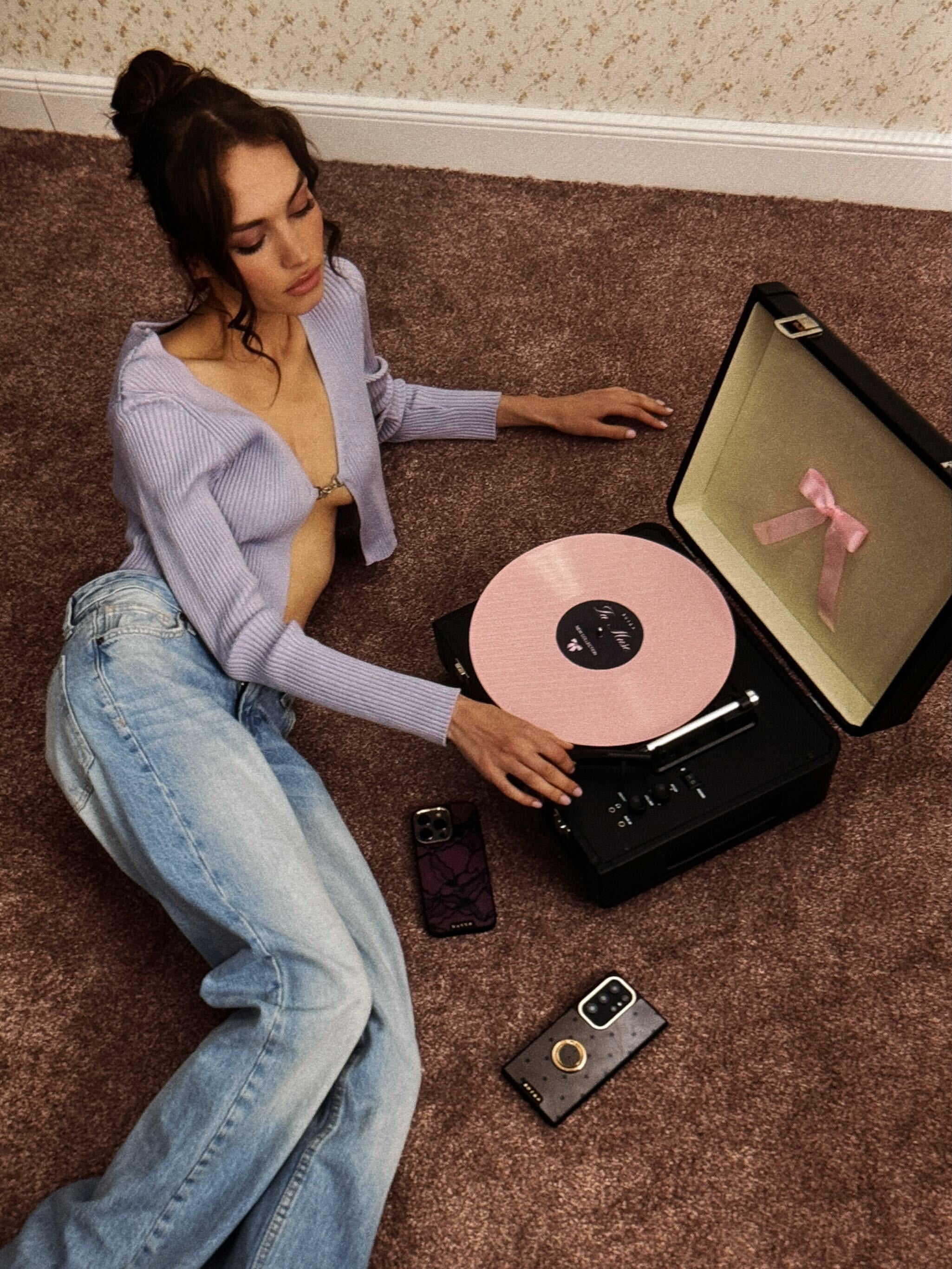 Woman relaxing on the floor with a pink record player, phones featuring BURGA cases nearby.