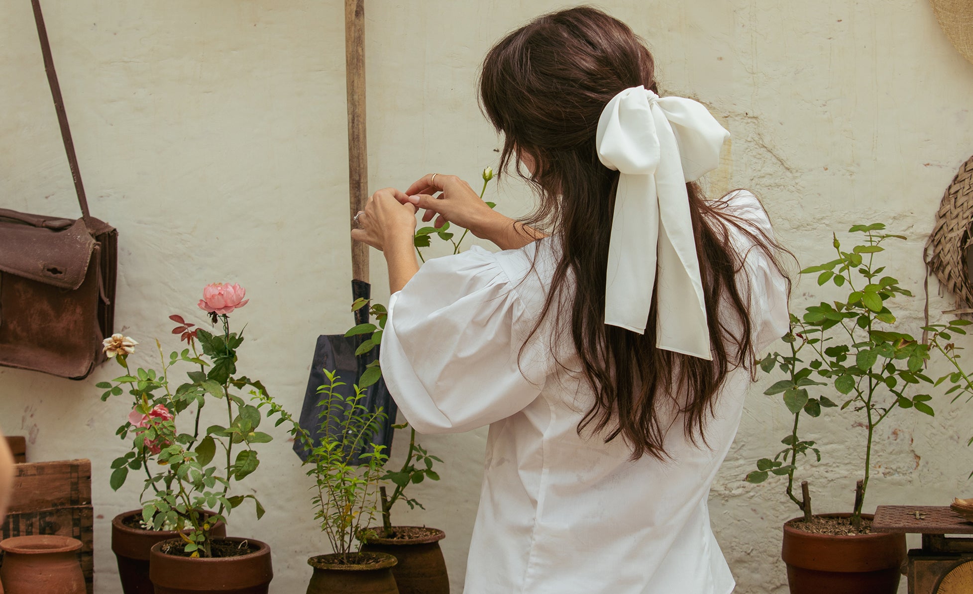 Woman in white blouse tending to plants in a rustic garden.