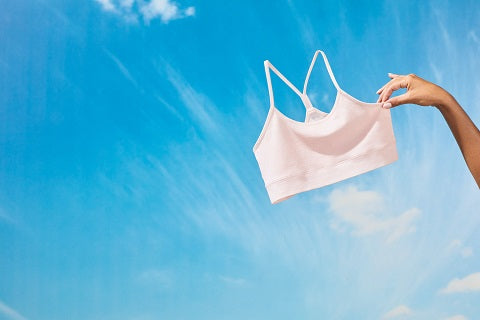 Womans hand holing wireless bamboo bra in the air with blues skies background