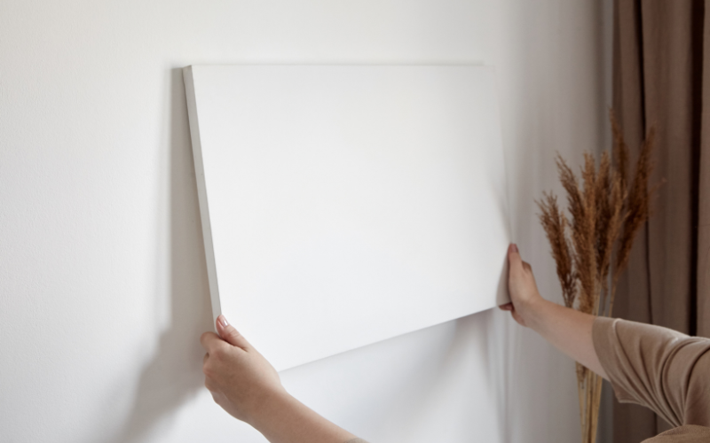 woman hanging canvas on white wall