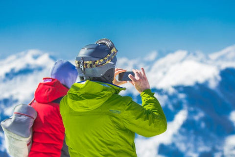 Mann in grüner Jacke und grauem Helm hält Telefon im Schnee