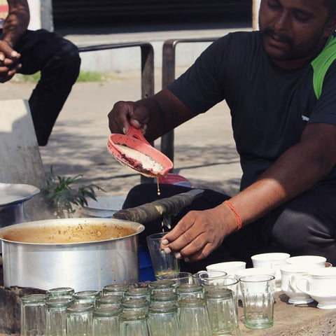 man pouring chai into glasses, at a tea stand in india