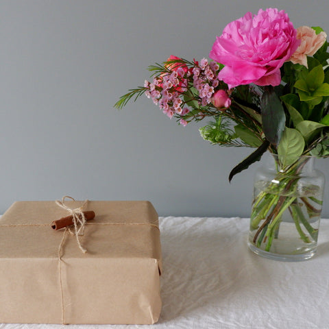 Wrapped Chai Walli gift in kraft paper, next to a bouquet of pink flowers.