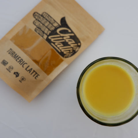 Chai Walli turmeric latte packet on a table with a glass of orange turmeric latte.