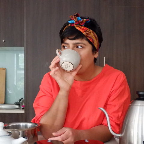 Uppma in a red top drinking a cup of chai