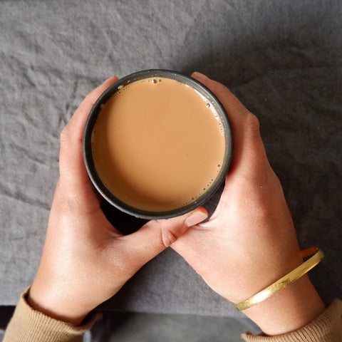 Two hands holding a cup of milky chai. 