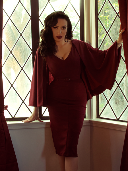 Micheline Pitt looking devilishly sexy standing in front of sundrenched windows while modeling a blood red goth outfit.