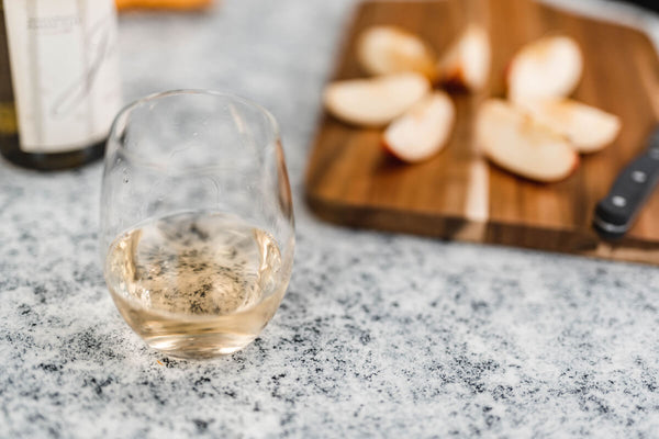 Glass of white wine, bottle and cut up apple on a countertop painted with the Giani Granite White Diamond Kit.