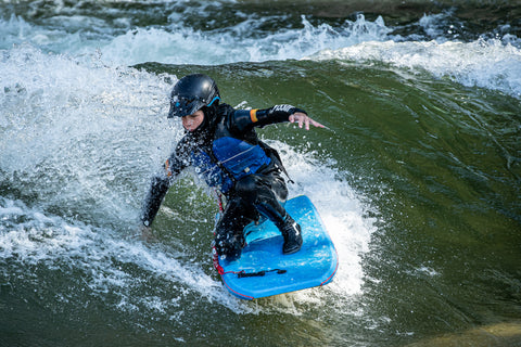 A young person surfing a body board on the Scout Wave in Salida, Colorado.