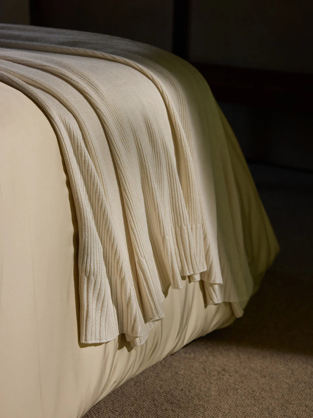 Beige ribbed knit blanket draped over the edge of a bed.