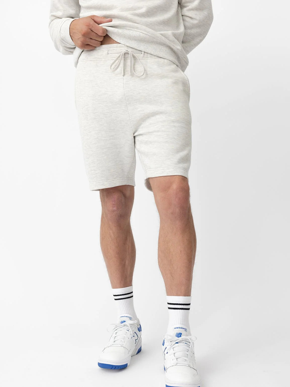 Person in grey shorts and white sneakers with white socks. Only lower torso visible.