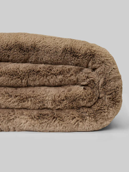 A rolled-up, fluffy, brown blanket against a gray background.