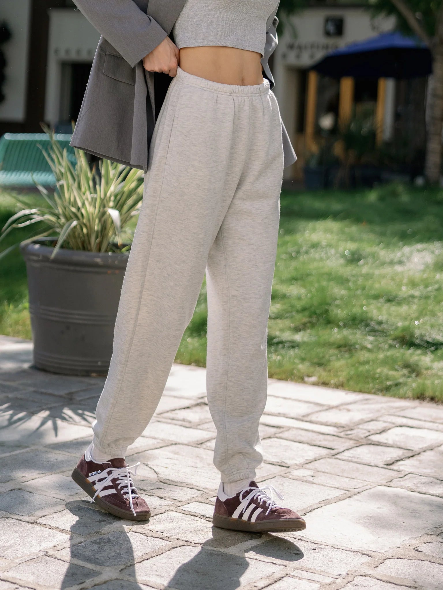Close-up of person's midsection wearing gray sweatpants and burgundy sneakers, with one hand on hip.