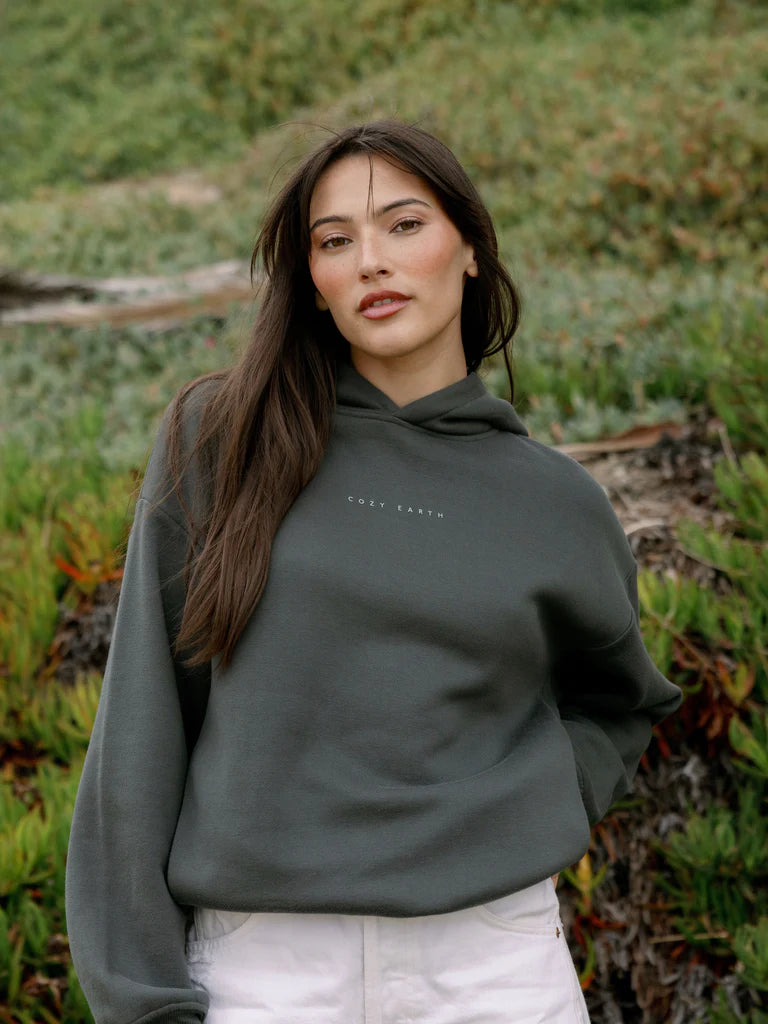 Woman in a hoodie standing in front of greenery.
