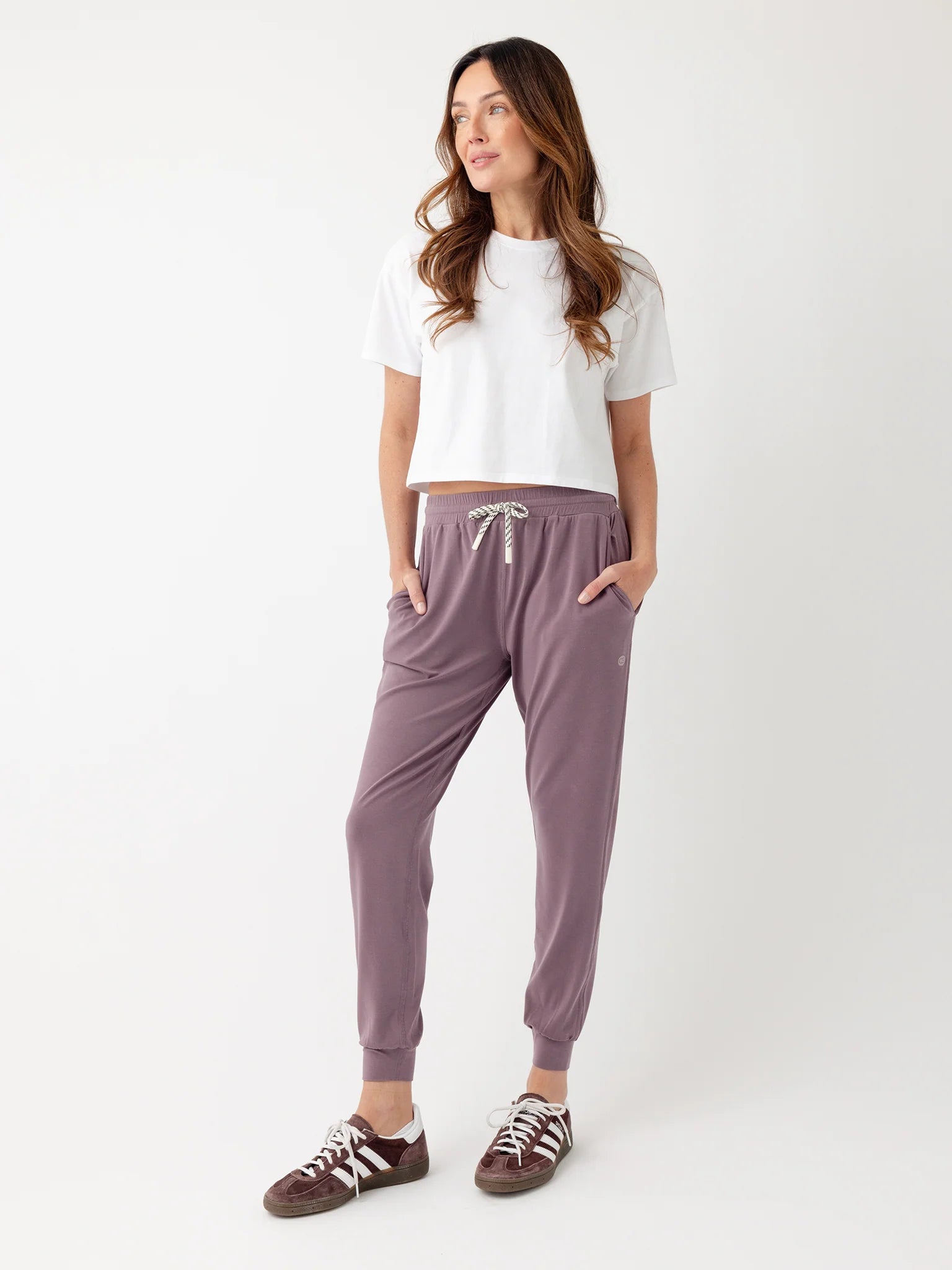 Woman wearing a white crop top and purple jogger pants with sneakers.