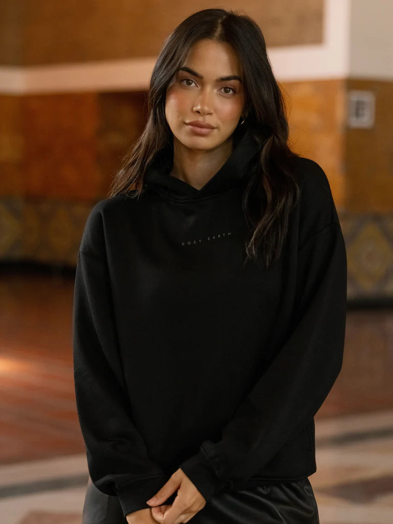 Woman in a black hoodie standing indoors.