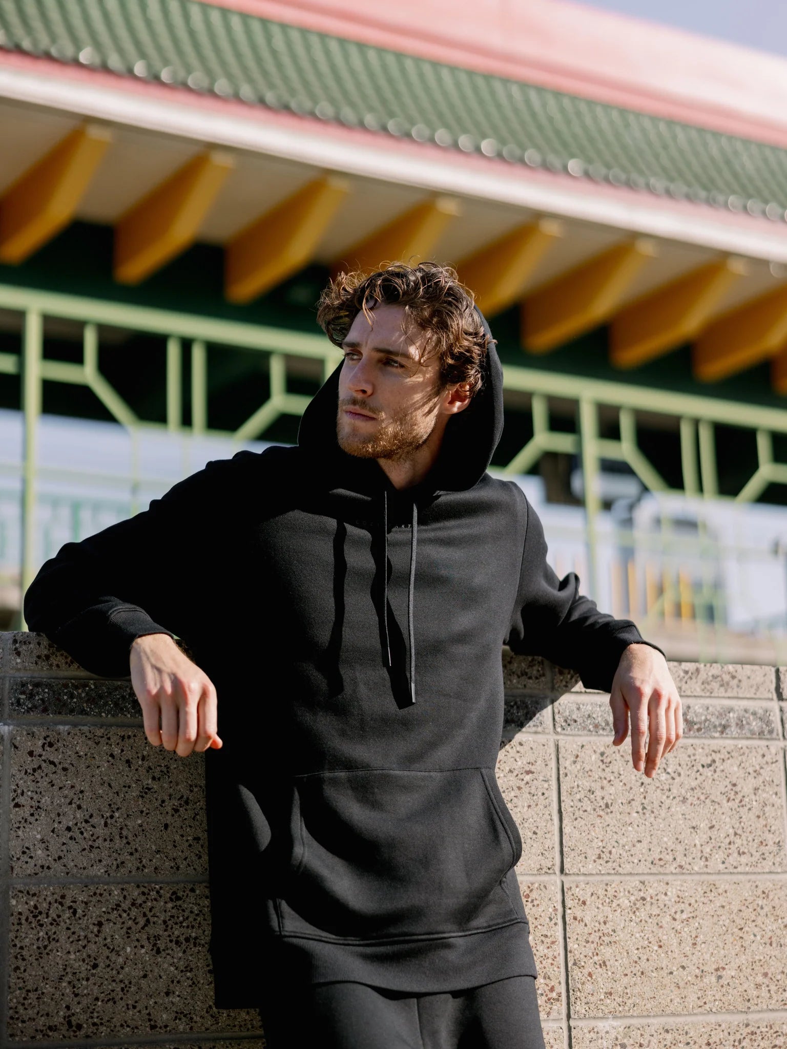 Man in black hoodie leaning on a wall with an Asian-style building in the background.