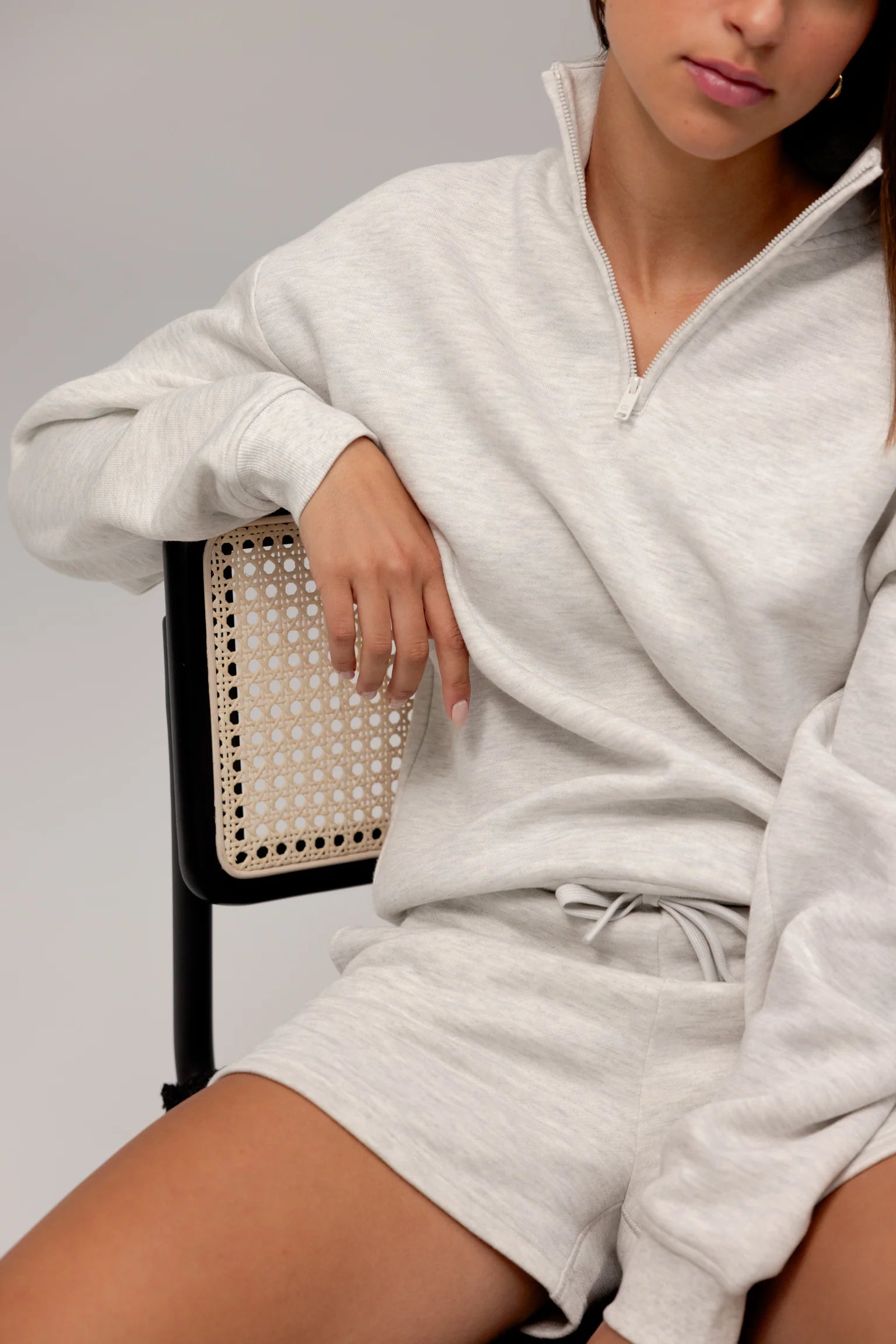 Woman in a casual grey sweatshirt and shorts sitting on a chair.