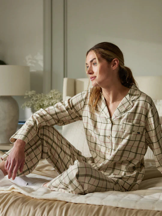 Person in plaid pajamas sitting on a bed, looking contemplative.