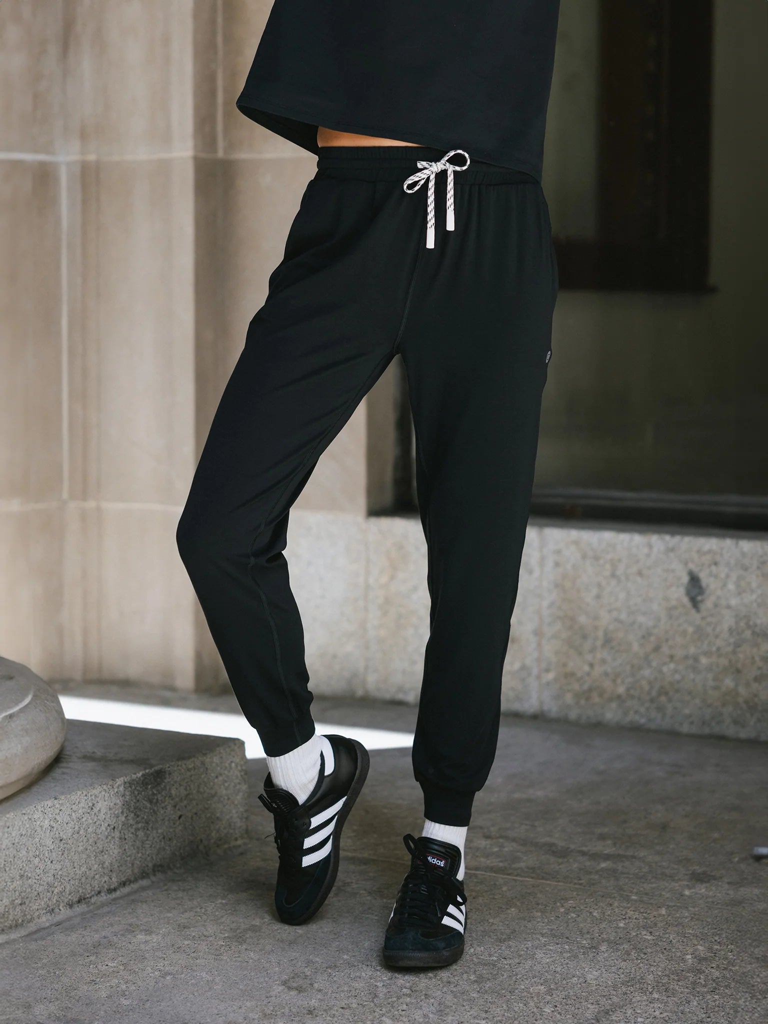 A person wearing black joggers with a drawstring and black Adidas sneakers.