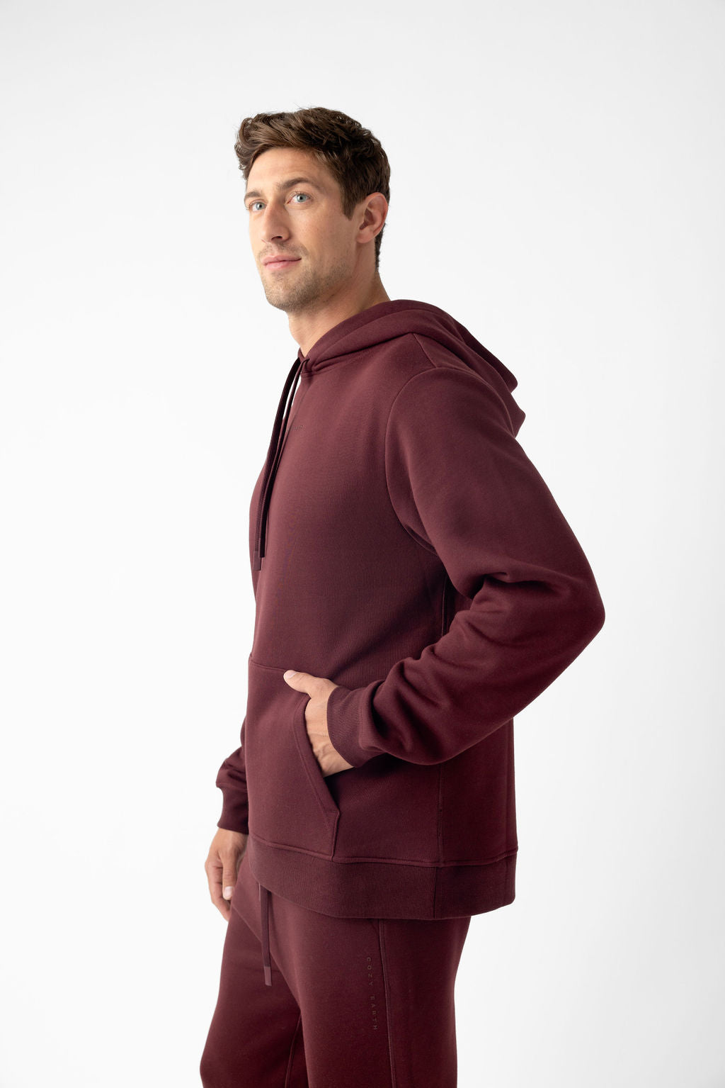 Man wearing a maroon hoodie and matching sweatpants, posing against a plain background.