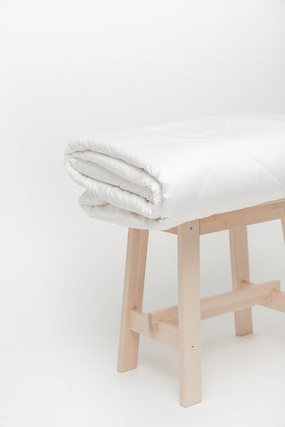 Cozy Earth white duvet folded on top of natural-colored stool
