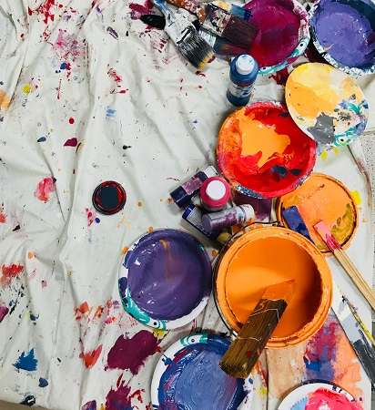 Paint cans, paintbrushes, and paint splatters on an old sheet or cloth