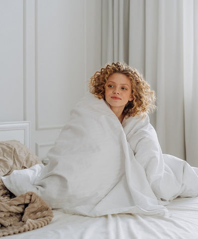 Young woman wrapped in a comforter on a bed