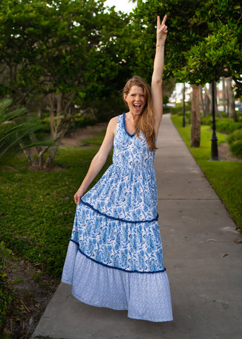 Woman wearing blue and white maxi dress holding up peace sign