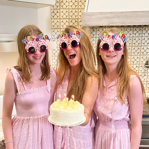 Women in pink dresses with sunglasses on holding birthday cake