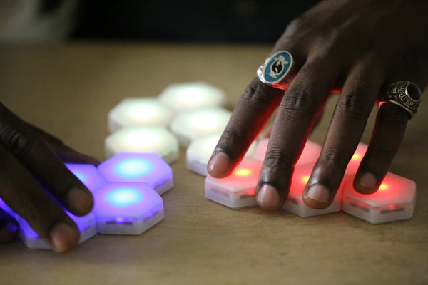 Black hands splitting magnetic, hexagonal and glowing game pieces that are segregated into blue, yellow, and red