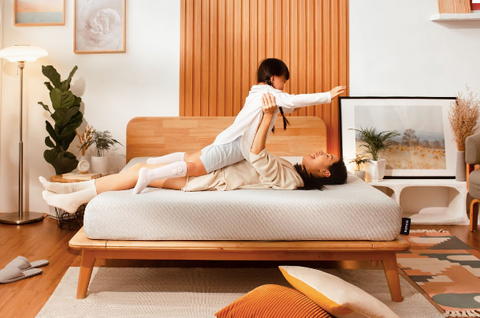 A woman playing with her child on a Sonno wood bed frame, surrounded by furniture and other decoration