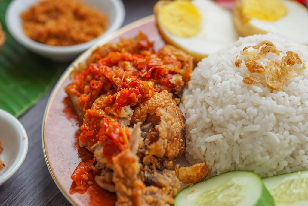 A plate of nasi lemak, surrounded by eggs, meat, cucumbers and sambal