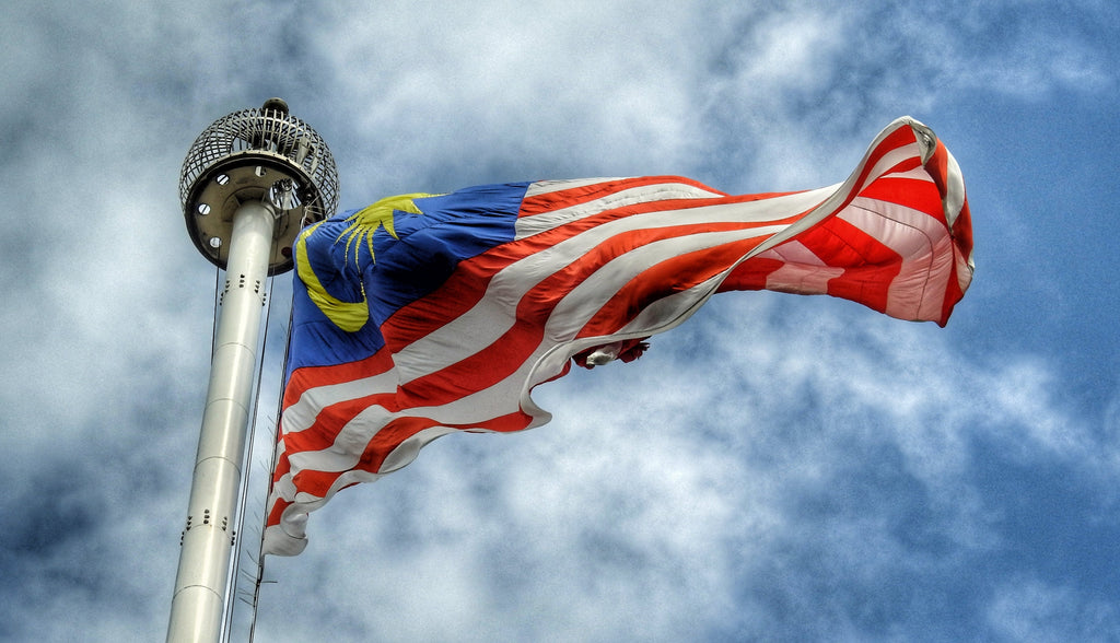 A Malaysian flag, or Jalur Gemilang, flying in the wind against a blue sky