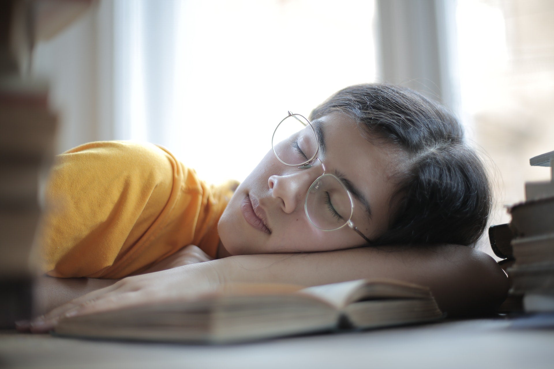  A girl asleep with her head resting on her hands on top of an open book