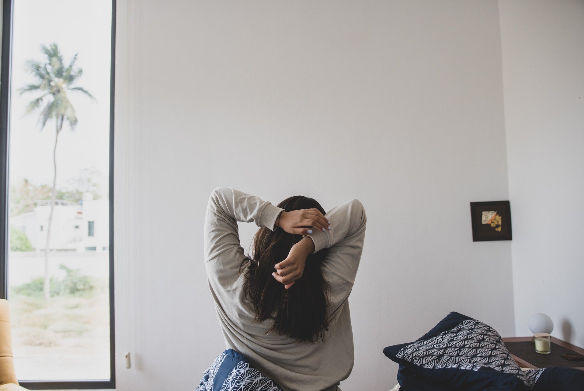  A girl sitting on top of her bed, stretching her hands behind her back, in her room.
