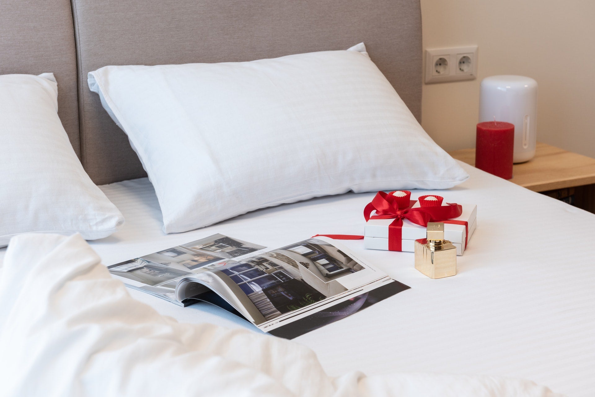 Presents, both wrapped and unwrapped, next to a magazine laid out on a white bedspread atop of a white bed in a room