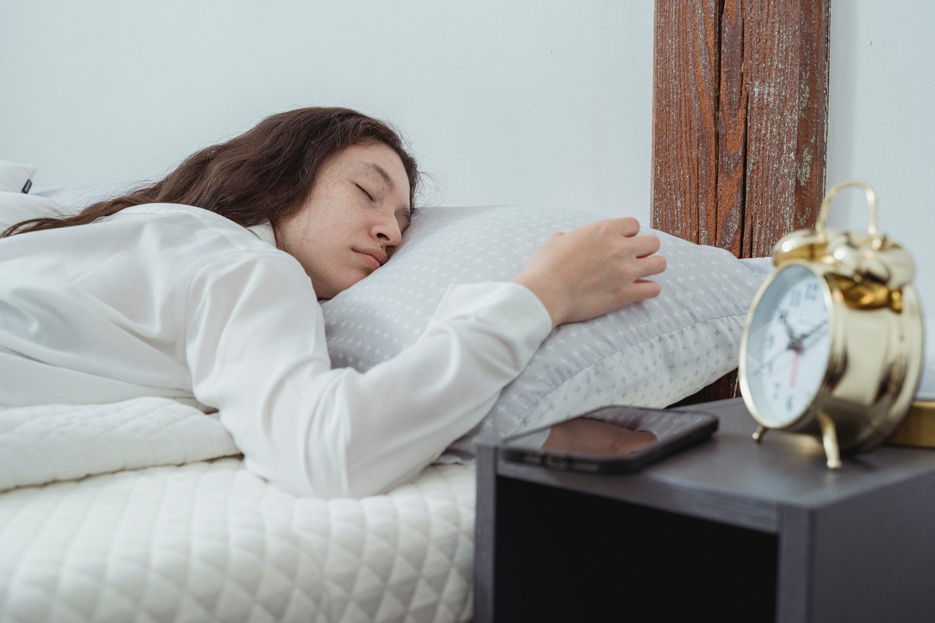 A girl asleep in bed, with her phone next to her on her bedside table
