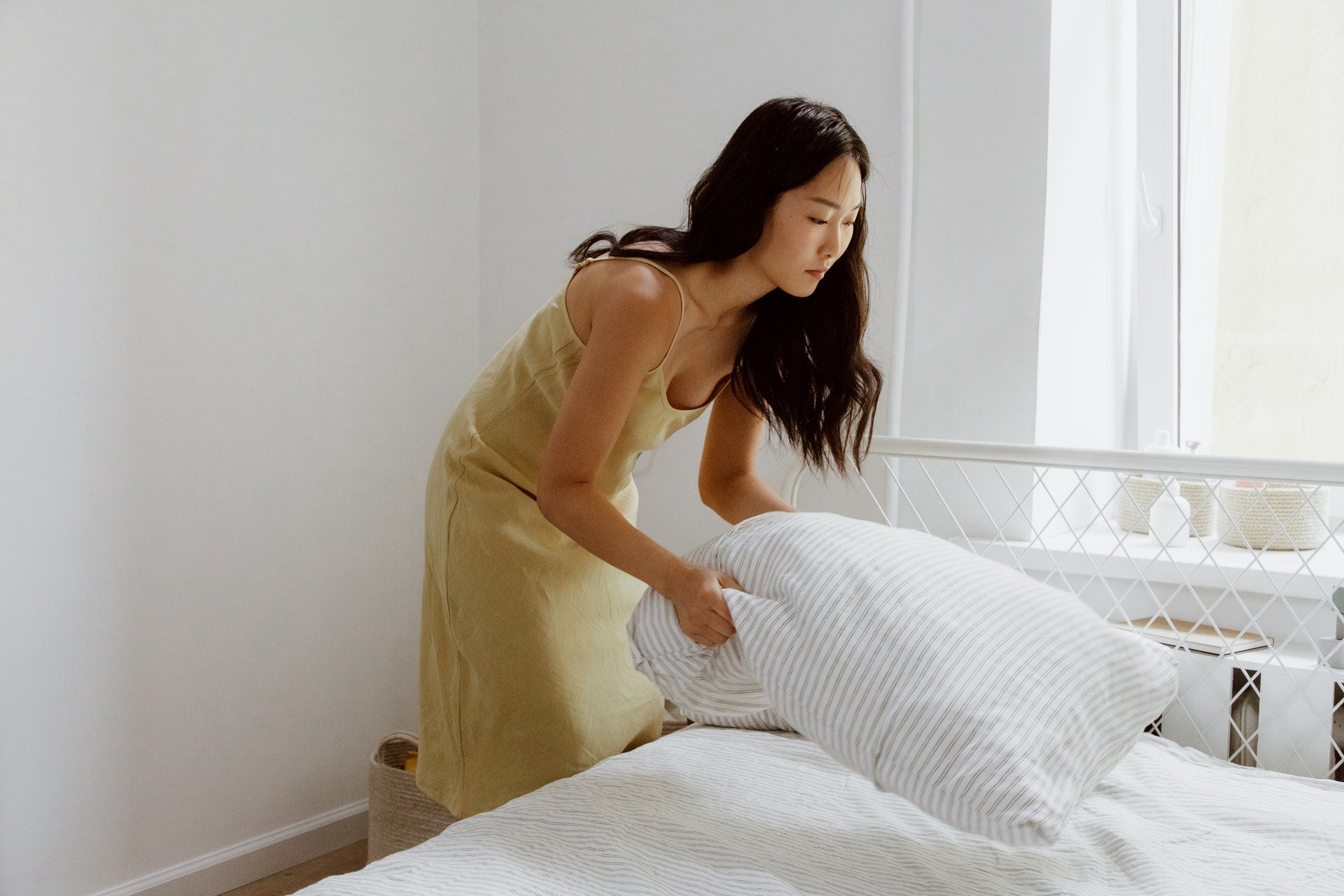 A girl fluffing her striped pillowcase before laying it onto her white bed