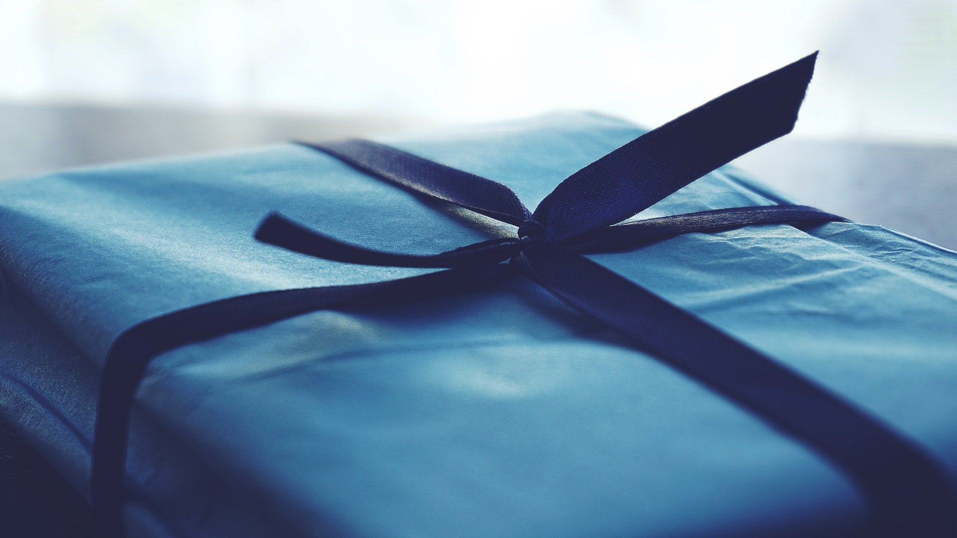 A gift wrapped in blue wrapping paper with a dark blue ribbon