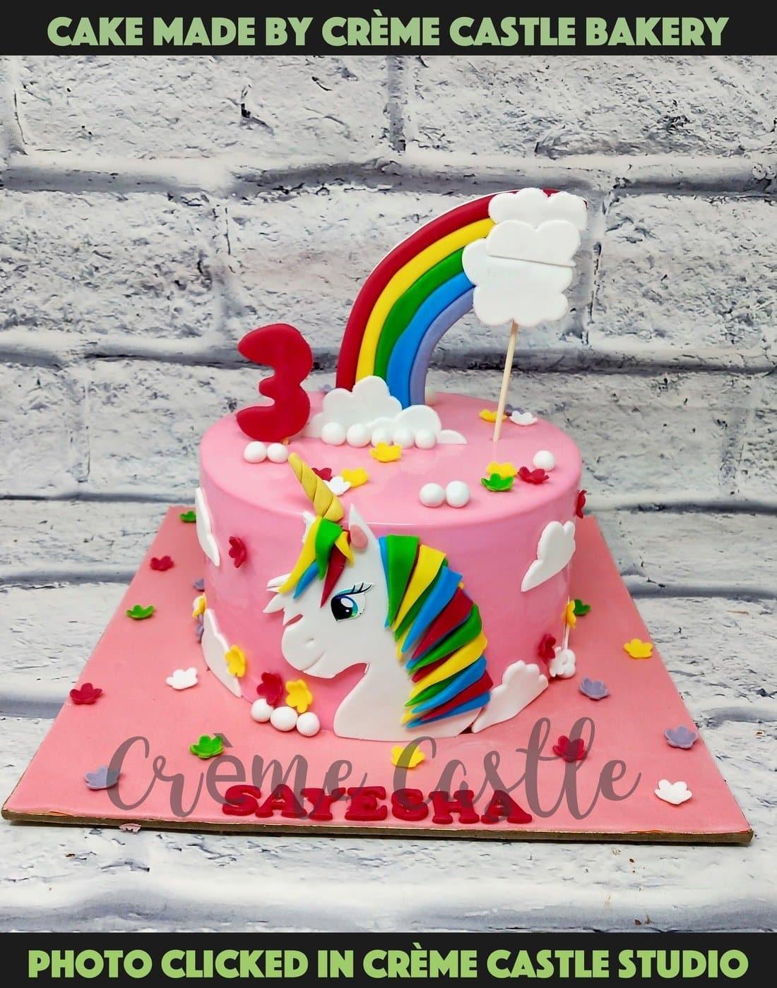 A pink color cake a beautiful unicorn in front and a rainbow on ...