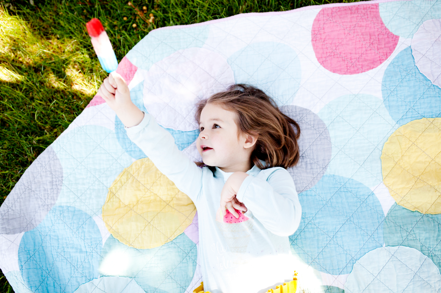 A toddler lying on a picnic blanket in the summer and holding a yogurt popsicle. Concept of summer, toddlers, healthy snacks.