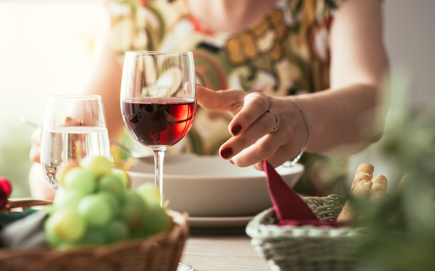 A woman reaches for a glass of wine on the dinner table. Concept of pregnant women avoiding foods like alcohol.
