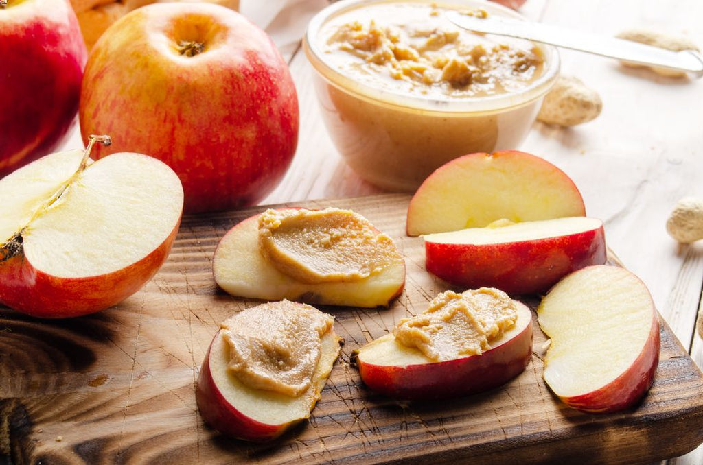 Apple slices covered in peanut butter lying on a chopping board as a healthy halloween snack for toddlers. 