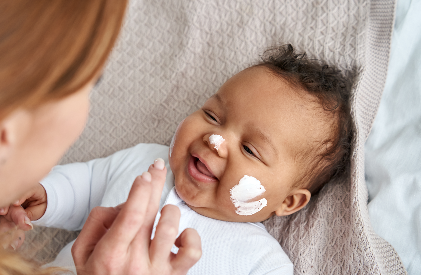 A mother applies an organic baby product or cream to her baby's cheeks. 