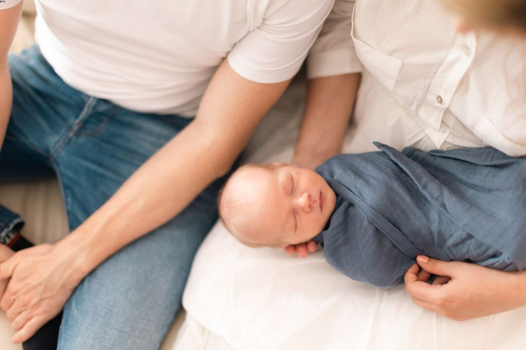 Parents holding a sleeping baby swaddled with a blanket