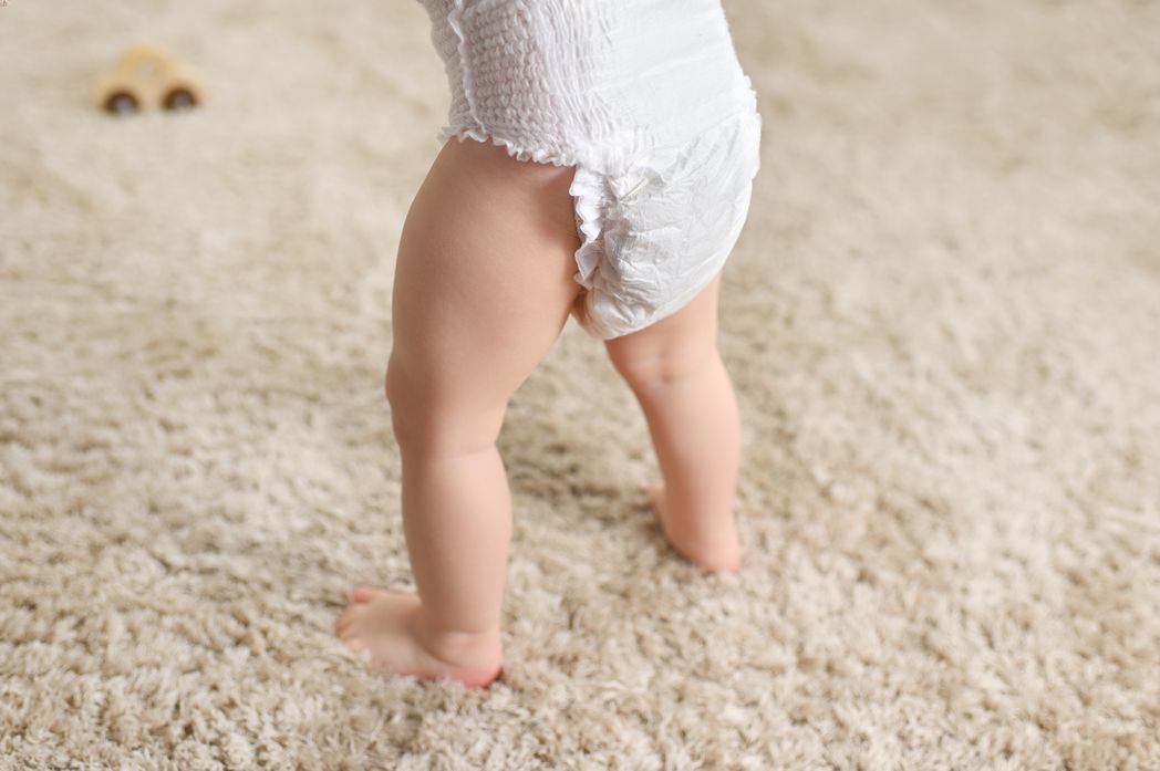 A baby in a diaper standing on a soft, fluffy carpet.