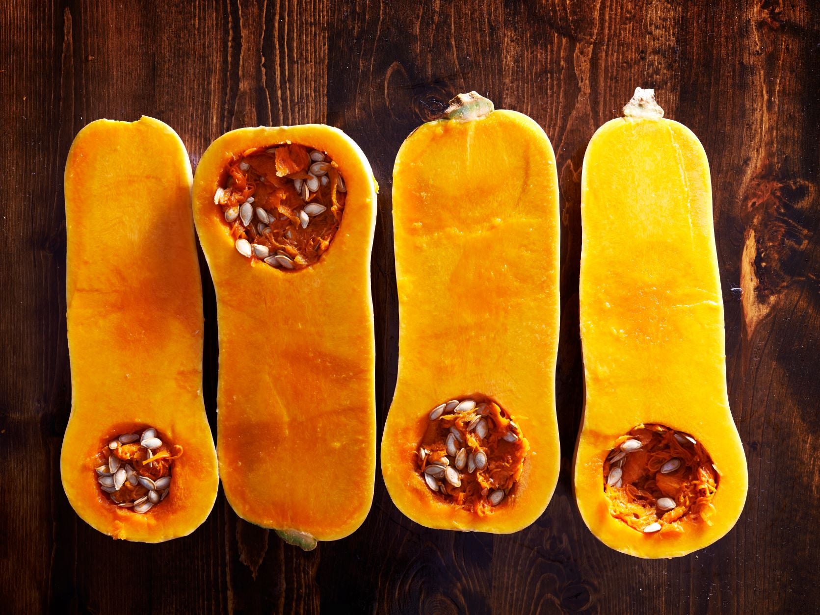 Four sliced halves of butternut squashes on a wooden surface. Butternut squash is a good first food for babies.