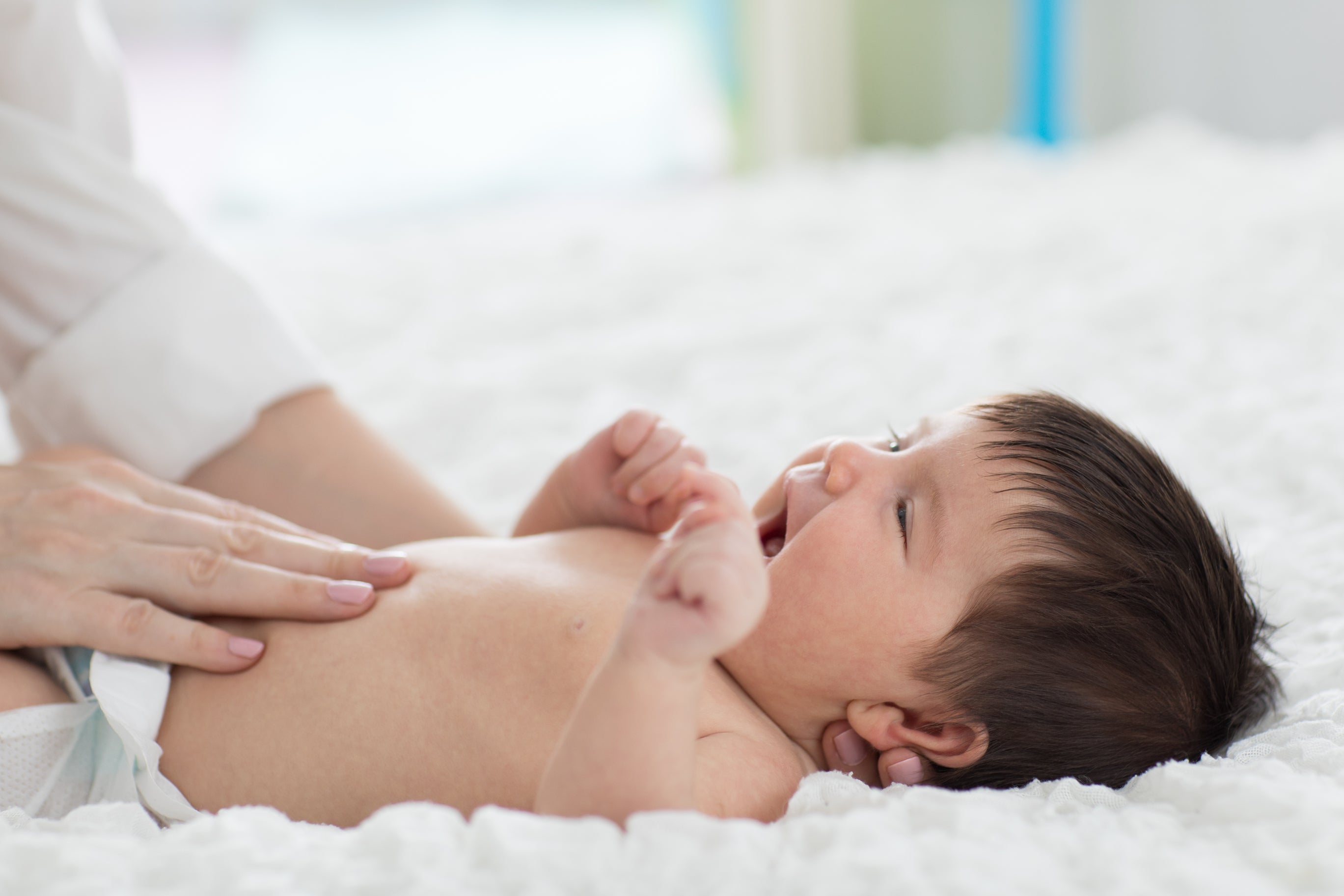 A mother applying baby lotion on her baby's tummy. Baby is lying on the bed. Concept of baby skin care, fragrance, fragrance free, harmful ingredients.